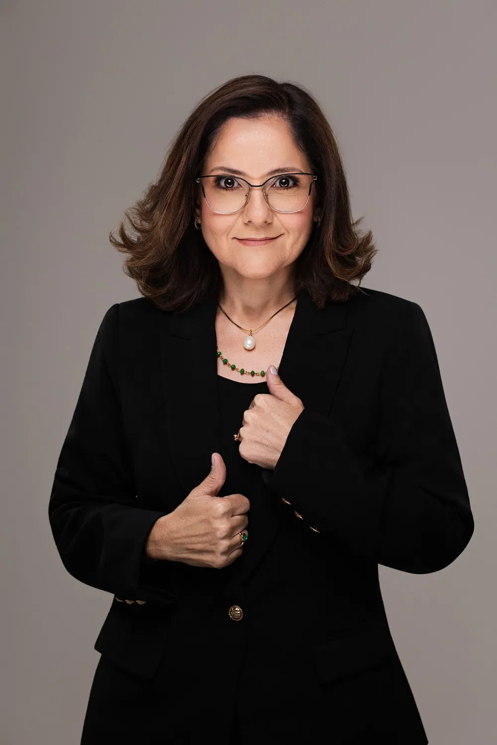 Adriana Muniz de blazer preto, sorrindo, com as mãos na lapela